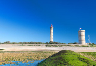 Zicht op vuurtorens en strand bij Flower Camping Les Ilates in Nouvelle-Aquitaine, Frankrijk, onder blauwe hemel.