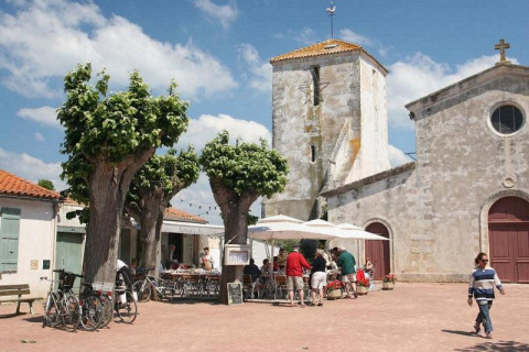 Mensen genieten op een zonnig terras tussen bomen en oude gebouwen in Loix, Nouvelle-Aquitaine, Frankrijk.