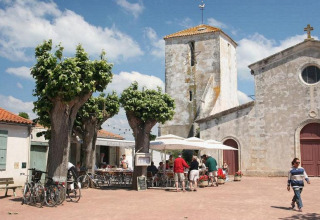 Mensen genieten op een zonnig terras tussen bomen en oude gebouwen in Loix, Nouvelle-Aquitaine, Frankrijk.