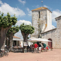 Menschen entspannen sich an einem sonnigen Tag im Café nahe historischen Gebäuden in Loix, Nouvelle-Aquitaine.