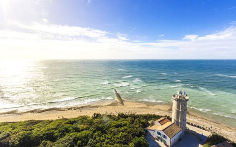 Kustzicht bij Loix, Nouvelle-Aquitaine, Frankrijk, met een oude vuurtoren en zonovergoten blauwe zee.