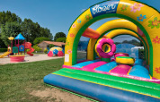 Legeplads med hoppeborg og rutsjebaner på Flower Camping Les Ondines, en feriepark i Occitanie, Frankrig.
