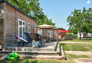 Houten chalets met terrassen, ligstoelen en parasols bij Flower Camping Les Ondines, Occitanië, Frankrijk.