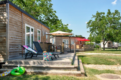 Houten chalets met terrassen, ligstoelen en parasols bij Flower Camping Les Ondines in Occitanie, Frankrijk.