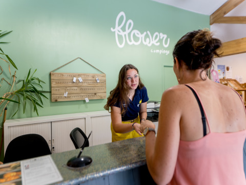 Receptioniste verwelkomt gast bij Flower Camping Les Ondines, een vakantiepark in Occitanië, Frankrijk.