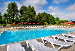 Outdoor swimming pool with sun loungers and red umbrellas at Flower Camping Les Ondines in Occitanie, France.