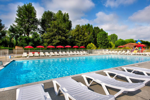 Outdoor swimming pool with sun loungers and red umbrellas at Flower Camping Les Ondines in Occitanie, France.
