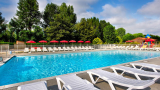 Outdoor swimming pool with sun loungers and red umbrellas at Flower Camping Les Ondines in Occitanie, France.
