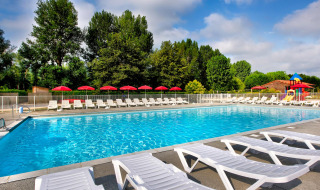 Outdoor swimming pool with sun loungers and red umbrellas at Flower Camping Les Ondines in Occitanie, France.