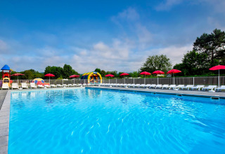 Piscina exterior con tumbonas, sombrillas rojas y zona de juegos en Flower Camping Les Ondines, Occitanie, Francia.