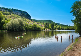 Personas nadando y en kayak en un río en Flower Camping Les Ondines, Occitania, Francia, rodeados de colinas verdes.