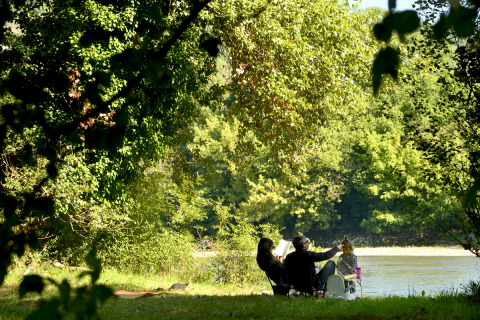 Mensen ontspannen aan de rivier onder bomen bij Flower Camping Les Ondines, Occitanie, Frankrijk.