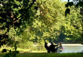 Persone che si rilassano vicino al fiume tra gli alberi al Flower Camping Les Ondines, Occitania, Francia.