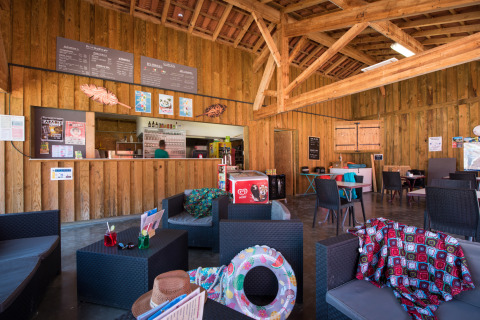 Zona de cafetería interior en Flower Camping Les Ondines, parque vacacional en Occitania, Francia, con asientos.