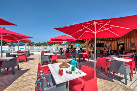 Buiten terras met rode parasols en stoelen bij Flower Camping Les Ondines, vakantiepark in Occitanië, Frankrijk.