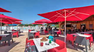 Outdoor terrace with red umbrellas and seating at Flower Camping Les Ondines holiday park in Occitanie, France.