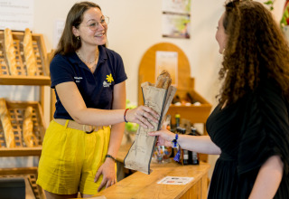 En medarbejder hos Flower Camping Les Ondines udleverer et brød til en gæst i receptionsområdet.
