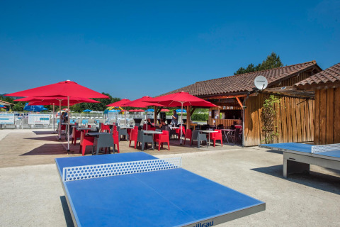 Zona de mesa al aire libre con sombrillas rojas en Flower Camping Les Ondines, Occitanie, Francia.