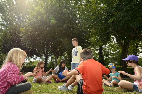 Kinderen spelen samen in een kring op het gras onder bomen bij Flower Camping Les Ondines, Occitanië, Frankrijk.