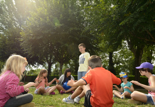 Kinderen spelen een kringspel op het gras onder bomen bij Flower Camping Les Ondines, Occitanie, Frankrijk.