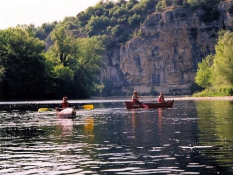 People canoeing on a calm river with lush trees and cliffs at Flower Camping Les Ondines in Occitanie, France.