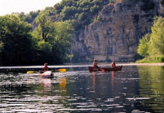 Mensen kanoën op een rustige rivier met bomen en rotsen bij Flower Camping Les Ondines in Occitanië, Frankrijk.