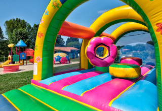 Farverigt hoppeborg og legeplads i Flower Camping Les Ondines, Occitanie, Frankrig, på en solrig dag.