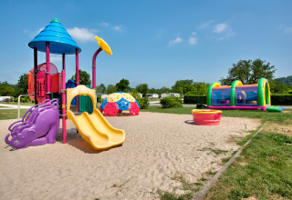 Legeplads med farverige legeredskaber og oppustelig hoppeborg ved Flower Camping Les Ondines i Occitanie.
