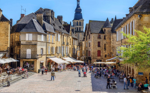 Plaza adoquinada animada en un pueblo francés, con cafés al aire libre y encantadores edificios antiguos.