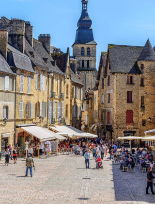 Place animée pavée dans une ville française avec terrasses de cafés et de charmants bâtiments en pierre.