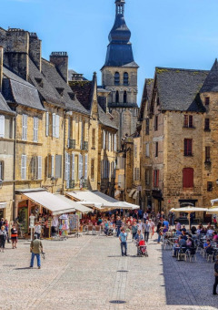 Bustling cobblestone square in a French town with outdoor cafés and charming historic stone buildings.