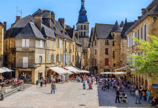 Bustling cobblestone square in a French town with outdoor cafés and charming historic stone buildings.