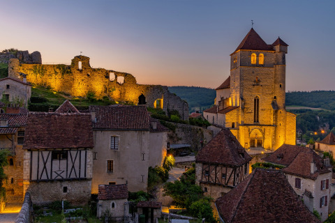 Vista al atardecer de casas de piedra y una iglesia iluminada en Flower Camping Les Ondines, Occitanie, Francia.