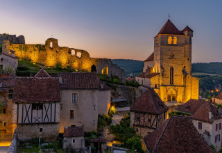 Solnedgang over gamle stenhuse og en oplyst kirke i Flower Camping Les Ondines, Occitanie, Frankrig.