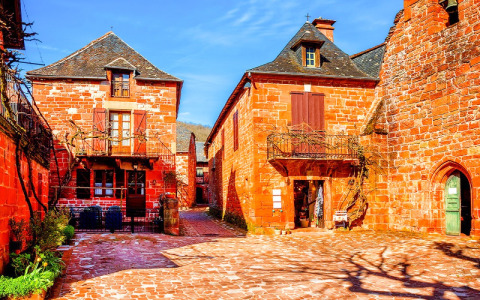 Edificios de piedra roja y cielo azul en Flower Camping Les Ondines, parque vacacional en Occitanie, Francia.