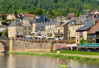 Foto del fiume e del pittoresco paese presso Flower Camping Les Ondines in Occitania, Francia, con persone in canoa.
