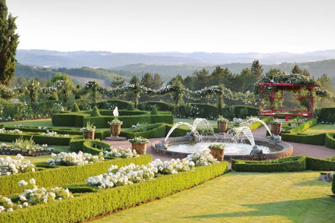 Jardín cuidado con setos, fuente y flores en Flower Camping Les Ondines, un parque en Occitanie, Francia.