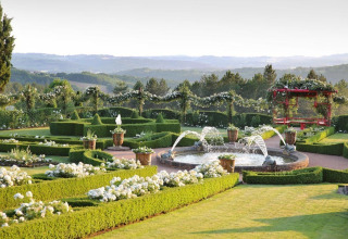 Jardin paysagé avec parterres fleuris, fontaine et verdure à Flower Camping Les Ondines en Occitanie, France.
