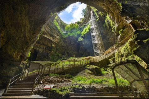 Ingang van de grot bij Flower Camping Les Ondines met trappen, zonlicht en groen in Occitanië, Frankrijk.
