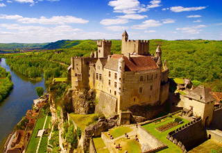 Aerial view of a castle perched on a cliff above a river near Flower Camping Les Ondines, Occitanie, France.
