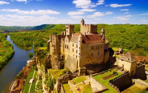 Aerial view of a castle perched on a cliff above a river near Flower Camping Les Ondines, Occitanie, France.