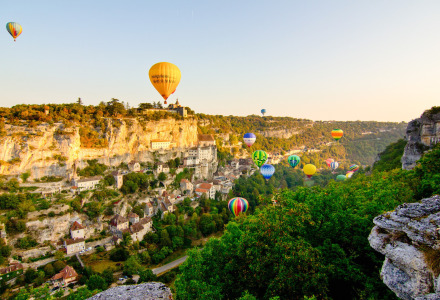 Colorful hot air balloons float over the scenic landscape surrounding Souillac in Occitanie, France.