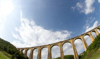 Photo of an impressive stone viaduct near Souillac in Occitanie, France, beneath a blue sky and surrounded by trees.