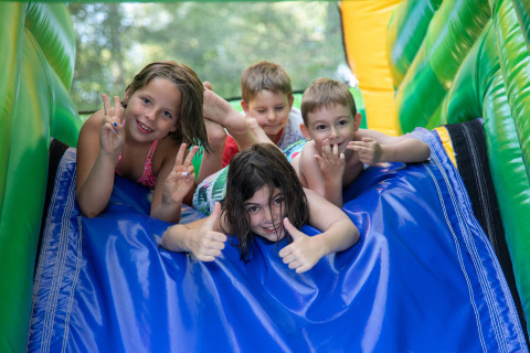 Kinder spielen und lachen auf einer Hüpfburg-Rutsche im Flower Camping La Plage, Nouvelle-Aquitaine, Frankreich.