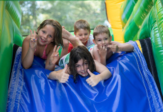 Kinder spielen und lachen auf einer Hüpfburg-Rutsche im Flower Camping La Plage, Nouvelle-Aquitaine, Frankreich.