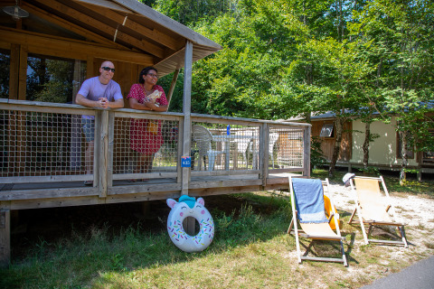 Zwei Personen entspannen sich auf der Veranda einer Holzhütte, mit Liegestühlen und Schwimmring davor.