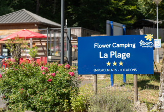 Blå skilt for Flower Camping La Plage feriepark i Nouvelle-Aquitaine, Frankrig, omgivet af blomster.