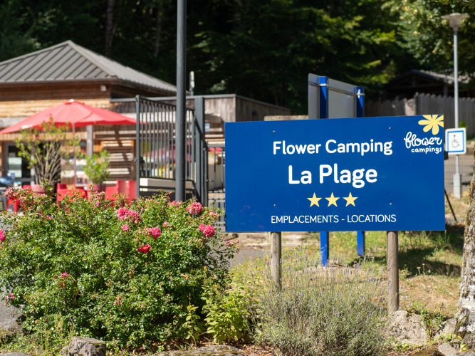 Blauw bord van Flower Camping La Plage vakantiepark in Nouvelle-Aquitaine, Frankrijk, tussen bloemen.