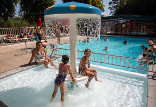 Kinder spielen unter einem Wasserpilz im Poolbereich von Flower Camping La Plage, Nouvelle-Aquitaine, Frankreich.