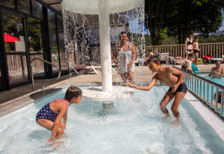 Children play under a waterfall in the pool at Flower Camping La Plage, a holiday park in Nouvelle-Aquitaine.